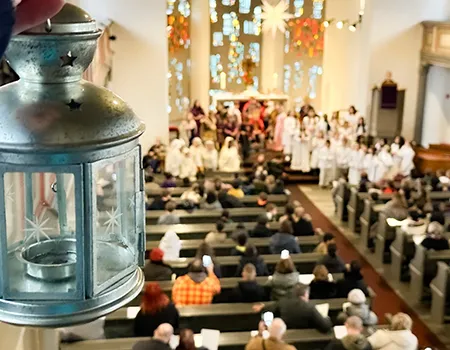 Stimmungsbild: Lampe im Kirchenraum im Vordergrund, im Hintergrund schemenhaft das Krippenspiel